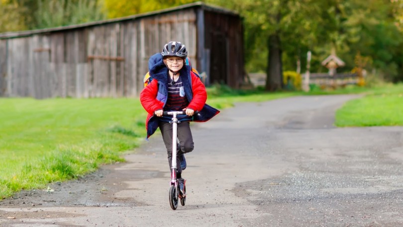 Ein Junge mit Helm und Schulrucksack fährt auf einem Tretroller. Ein Junge mit Helm und Schulrucksack fährt auf einem Tretroller.