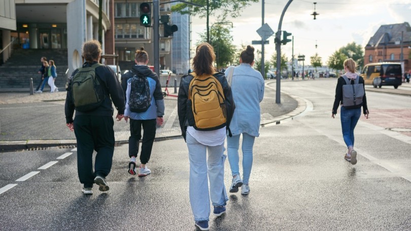 Rückansicht von fünf Personen, die bei grüner Fußgängerampel die Straße überqueren Rückansicht von fünf Personen, die bei grüner Fußgängerampel die Straße überqueren